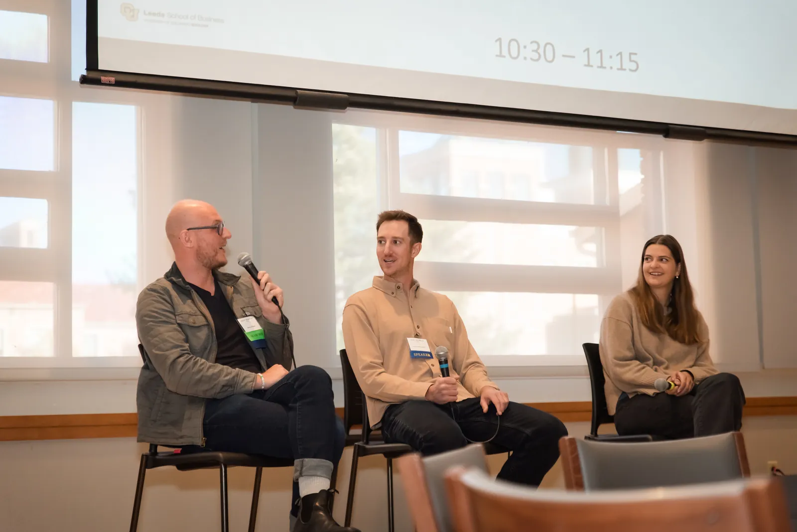 Three panellists seated in front of a window, one speaking into a microphone